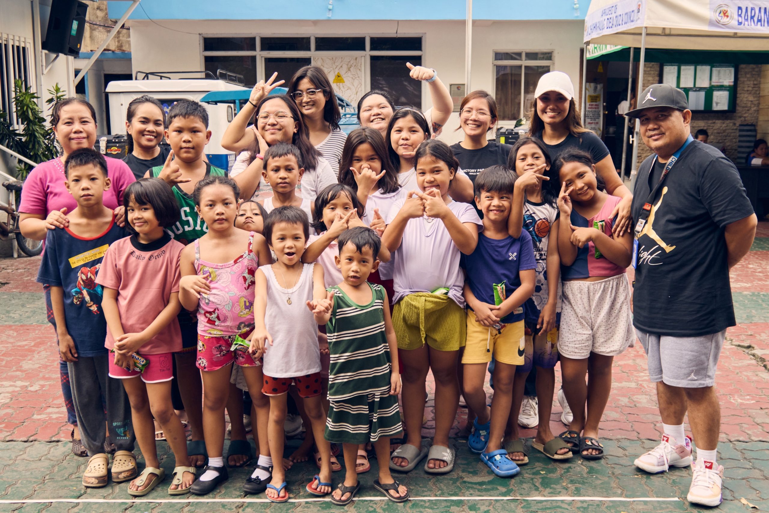 A group of smiling children and adults pose for a photo outside in a courtyard area.